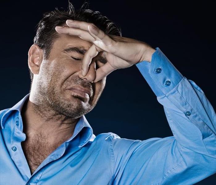 middle aged man with long sleeved blue shirt pinching his nose closed to avoid bad smell
