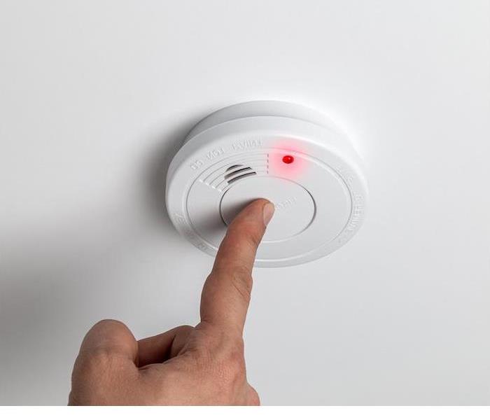 white fire alarm being tested by a person 